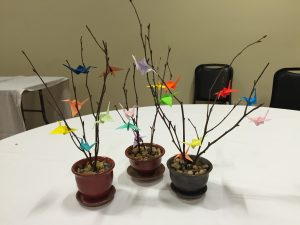 Dinner centerpiece of trees with colorful paper cranes. 